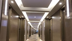 Un pasillo moderno de hotel con alfombra estampada, puertas de ascensor metálicas e iluminación empotrada.
