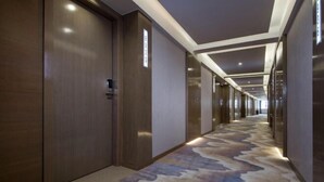 Un pasillo de hotel con puertas de madera, alfombra estampada e iluminación empotrada.