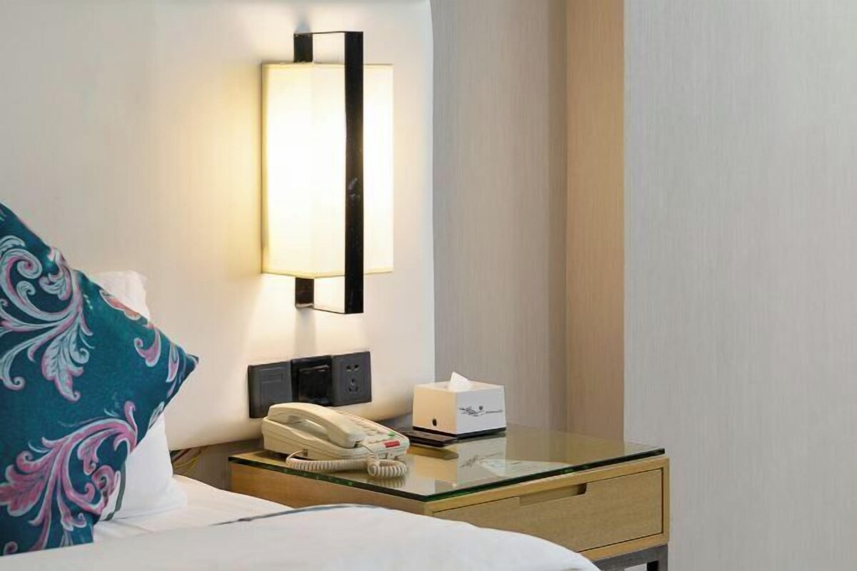 A hotel room with a bed, a bedside table with a telephone, a tissue box, and a wall-mounted light fixture.