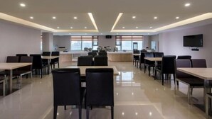 Un comedor moderno con varias mesas y sillas, una barra central y un televisor montado en la pared.