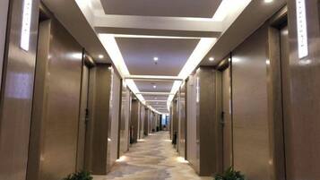 Corredor de hotel com piso revestido de carpete, portas de madeira e iluminação embutida.