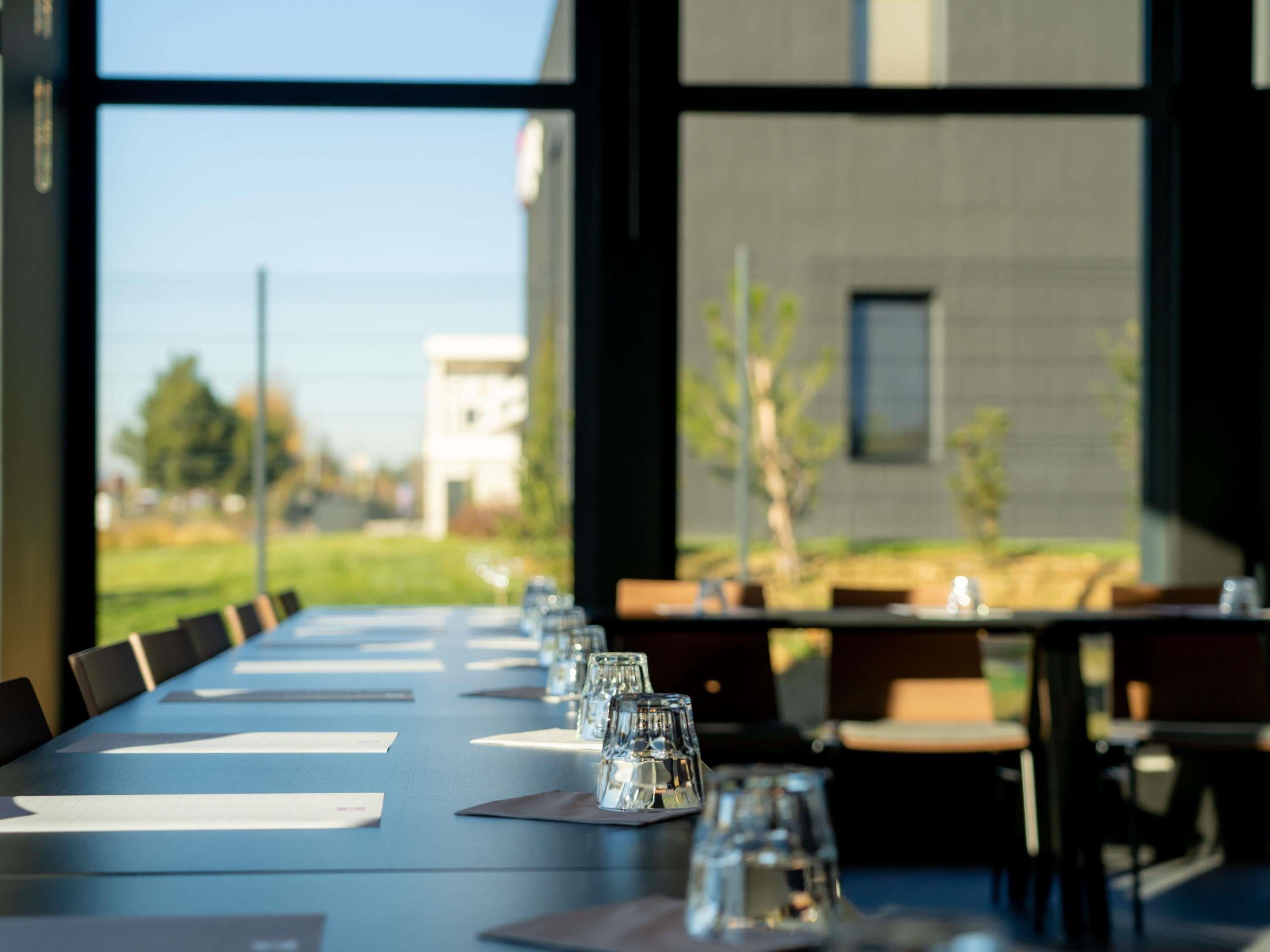 A conference table with chairs and water glasses, set against a backdrop of a building and a grassy area.