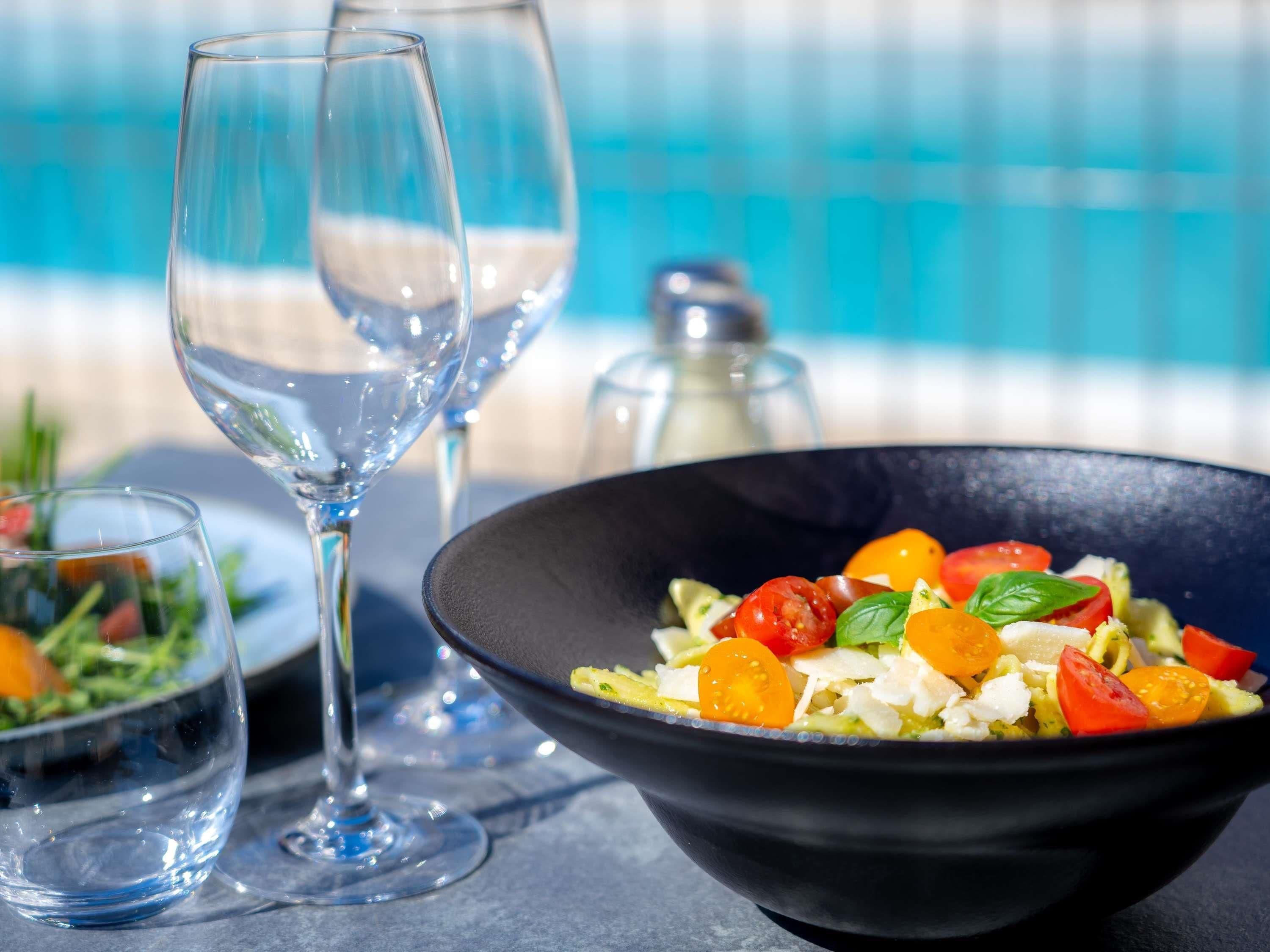 A dining table with a black bowl of salad, two wine glasses, and a salt shaker.