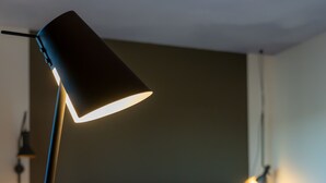 Un lit bien fait, avec du linge de lit blanc, une lampe de chevet et une petite table sur laquelle se trouvent un carnet ouvert et un stylo.