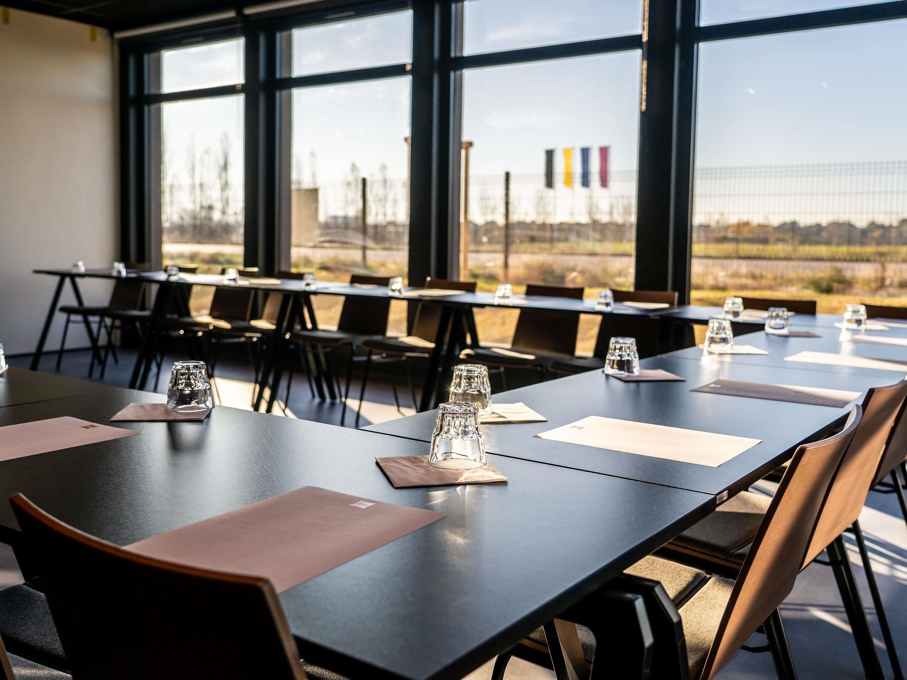 A conference room with tables and chairs, large windows, and a view of a distant landscape.