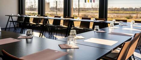 A conference room with tables and chairs, large windows, and a view of a distant landscape.