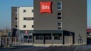 Un bâtiment moderne, facilement reconnaissable à son grand panneau rouge avec l’inscription « ibis », doté de nombreuses fenêtres et disposant d’un parking.