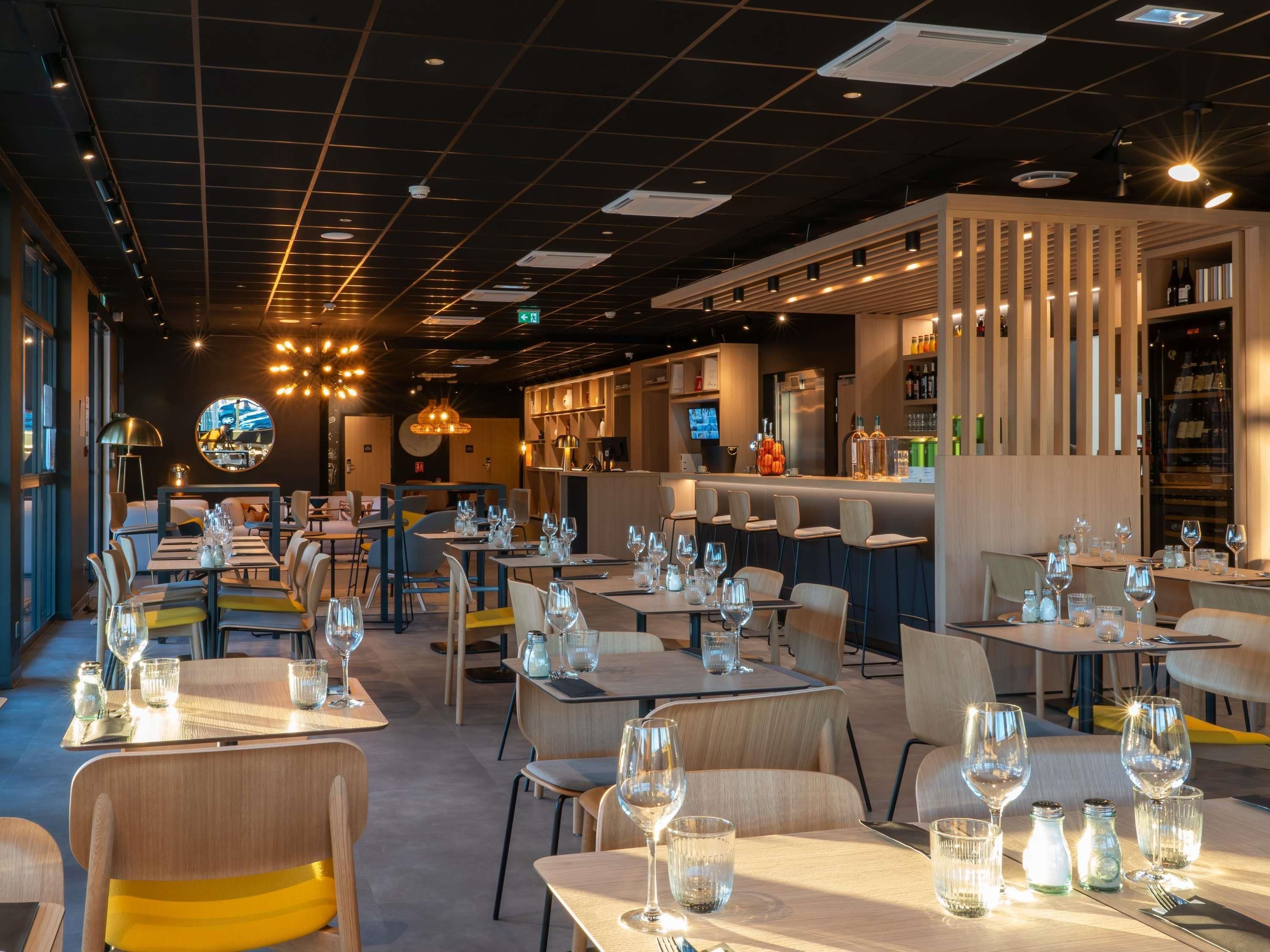 En restaurantindretning med flere spiseborde, stole og en bar.