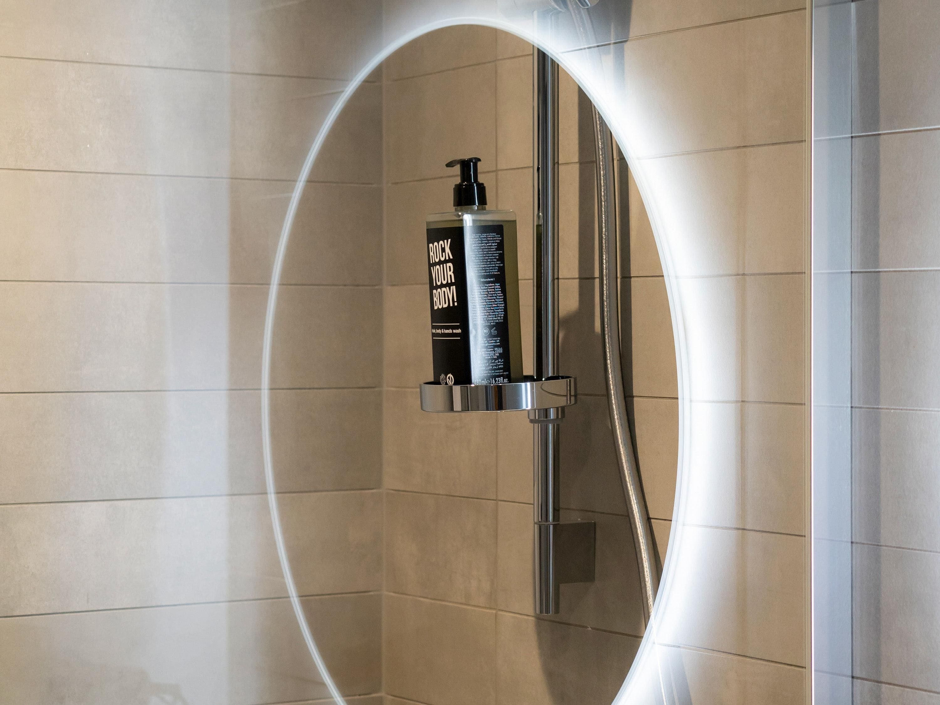 A bathroom with a shower enclosure, a hand soap dispenser, and a mirror.