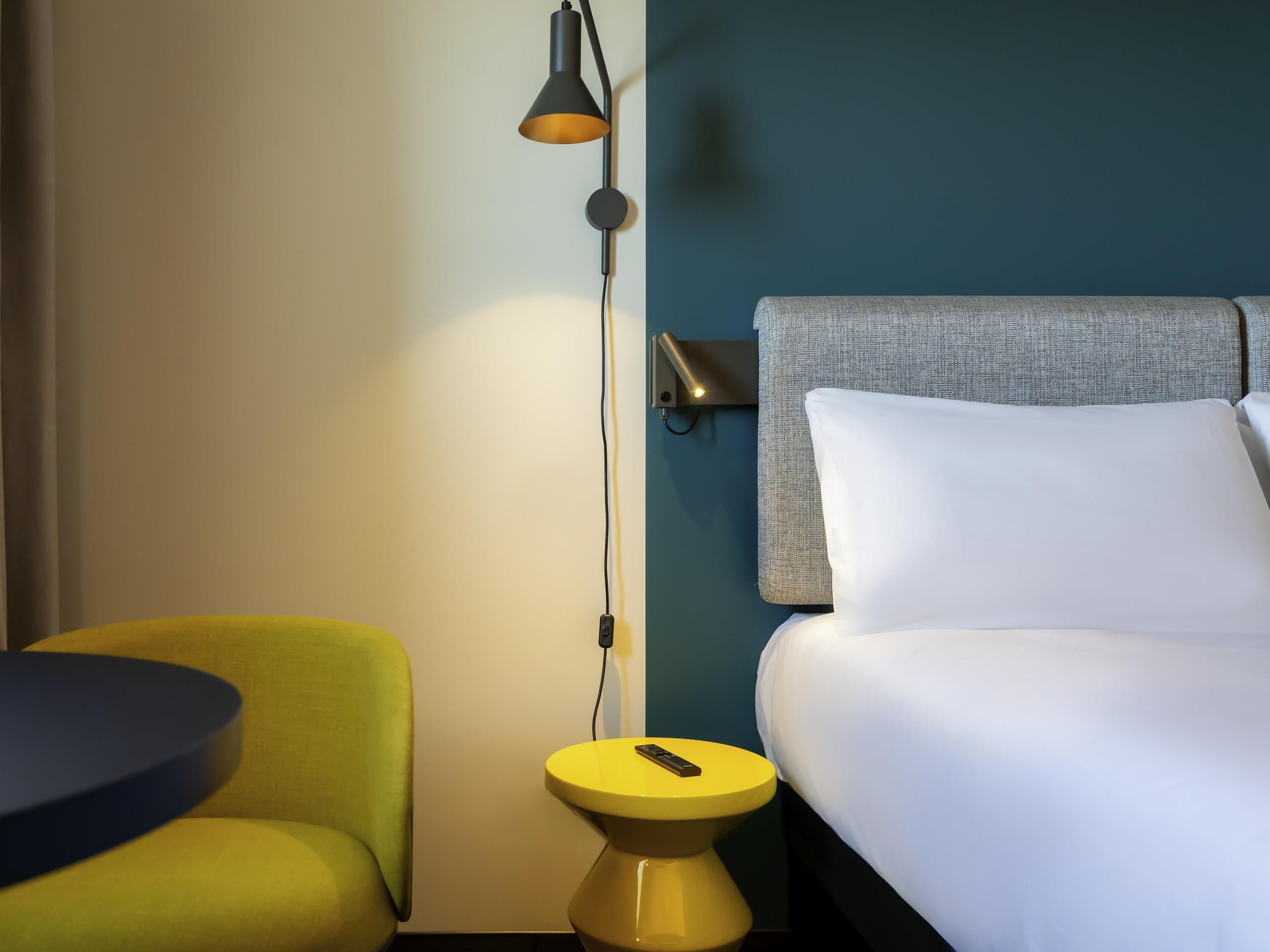 A hotel room with a bed, a bedside table with a lamp, a chair, and a small table.