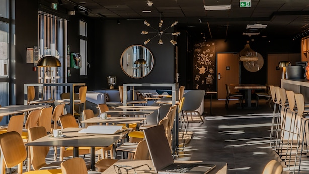 Un café moderne doté de nombreuses tables et chaises, d’un grand miroir et d’un luminaire au plafond original.