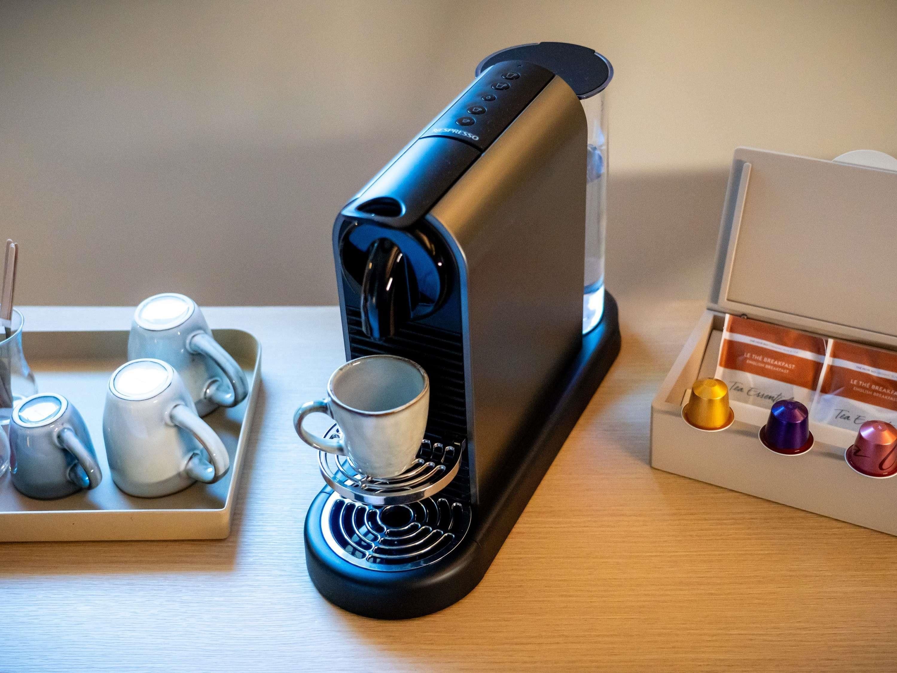 Una cafetera con una bandeja de tazas y una caja de cápsulas de té.