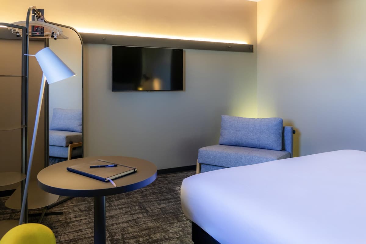 Habitación de hotel con cama, escritorio con silla, lámpara, televisor y sofá.