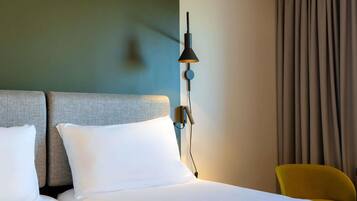 A hotel room with a bed, a nightstand, a lamp, a chair, and a curtain.