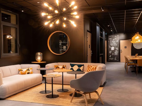 A modern interior with a sofa, armchairs, a round mirror, and a dining area.. ibis Saint Paul Trois Chateaux (Ouverture Decembre 23)
