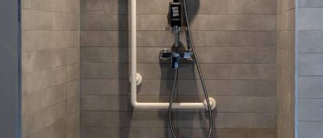 A shower area with a handheld showerhead, a wall-mounted control panel, and a white grab bar.