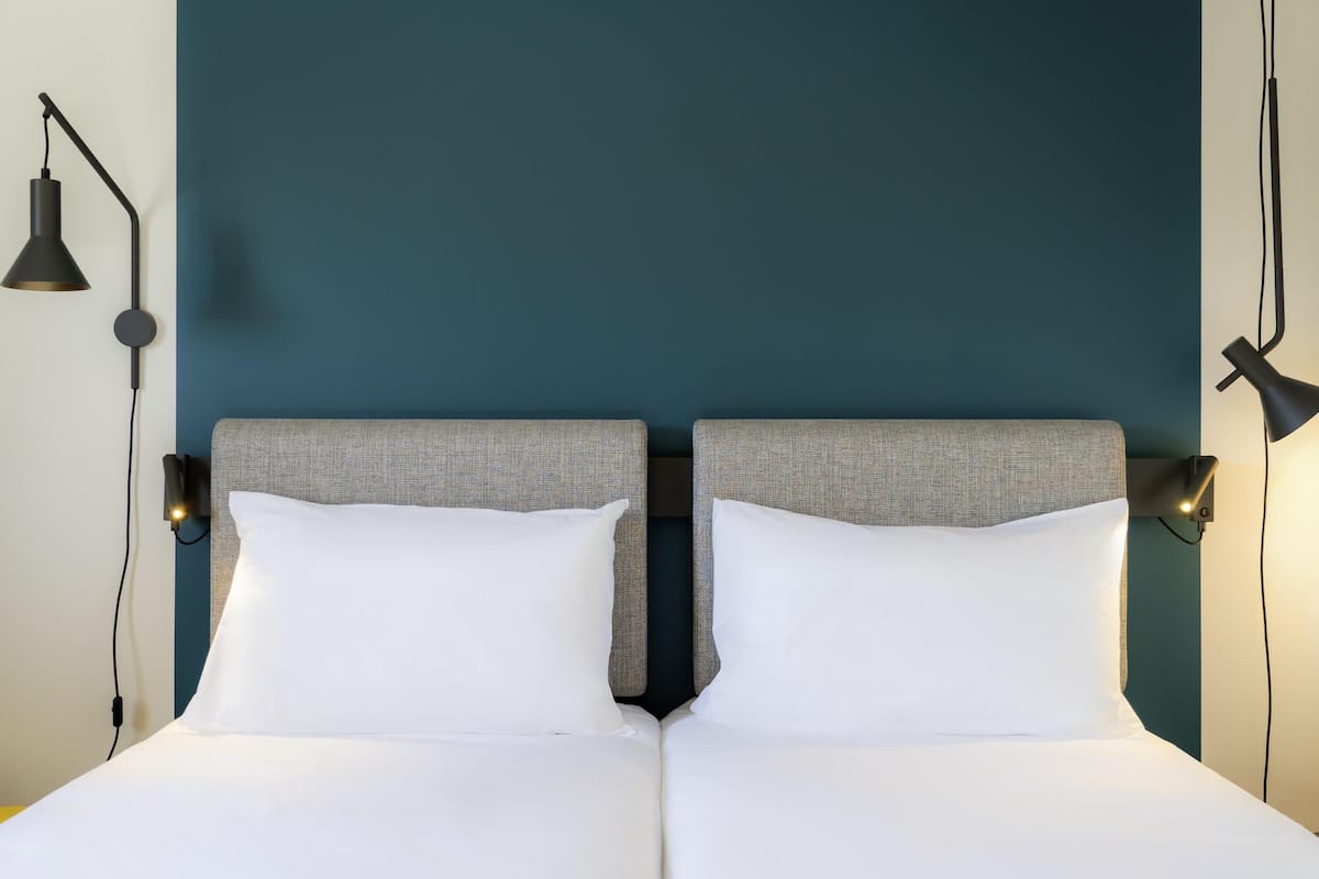 Una cama doble con dos almohadas, cabecero y dos lámparas fijadas a la pared.