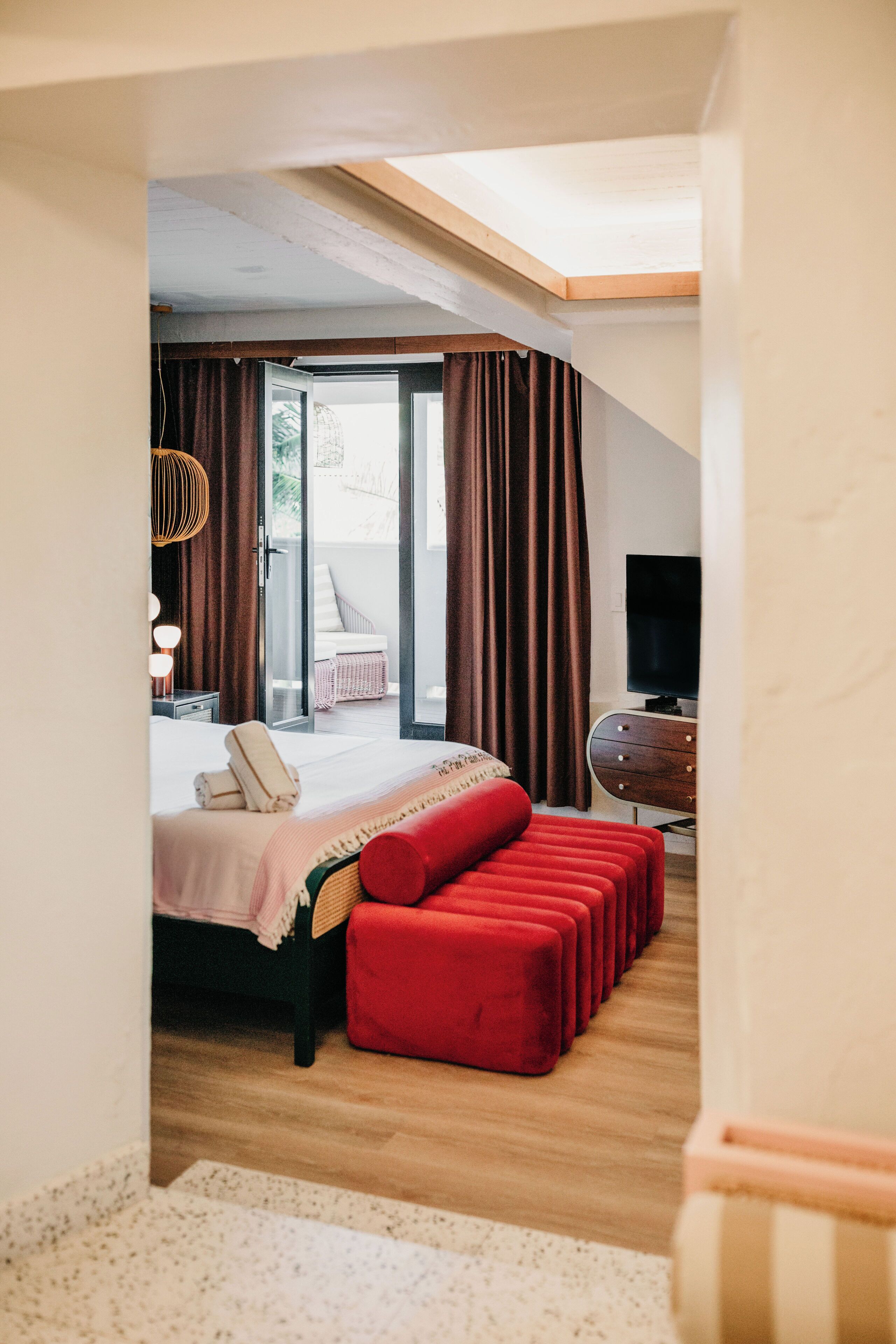 A bedroom with a bed, a TV, and a balcony with curtains.