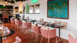 Ein Restaurantinneres mit Barbereich, rosafarbenen Sitzmöglichkeiten und einem großen Gemälde an der Wand.