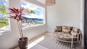 Ein Zimmer mit großem Fenster, einem Blumentopf, einer Couch und einer Pendelleuchte.