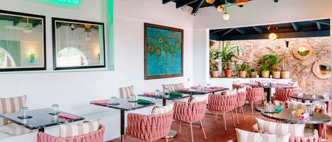 Interior de restaurante con varias mesas y sillas, un letrero de neón que dice 'EL BARSTO' y un mural en la pared.