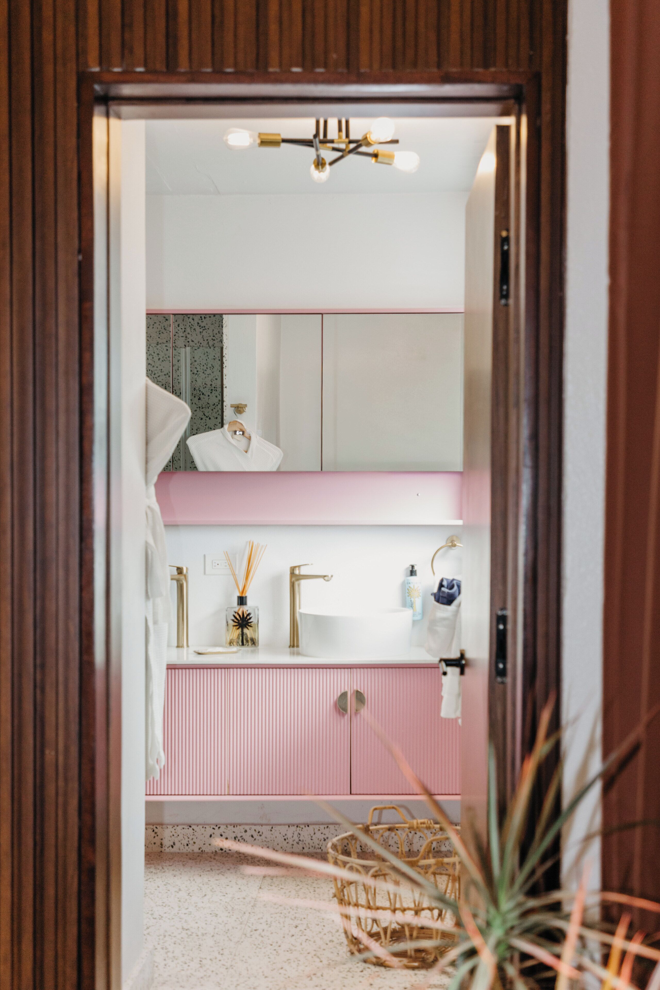 Une salle de bain avec un meuble-lavabo rose, un miroir et un luminaire au plafond.