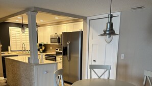 Una cocina moderna con armarios blancos, un refrigerador de acero inoxidable y un comedor con una mesa redonda y sillas blancas.