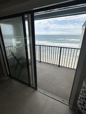 Un balcón con vista al océano, una puerta de vidrio y una silla.