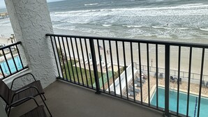 Un balcón con vista al océano, una piscina y mobiliario exterior.
