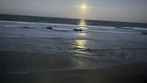 Escena de playa con olas y el reflejo de la luna visible en el agua.
