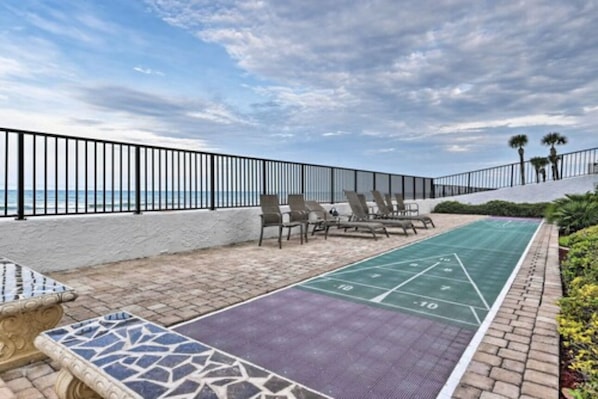 Zona de piscina con sillas de descanso y una cancha de shuffleboard.