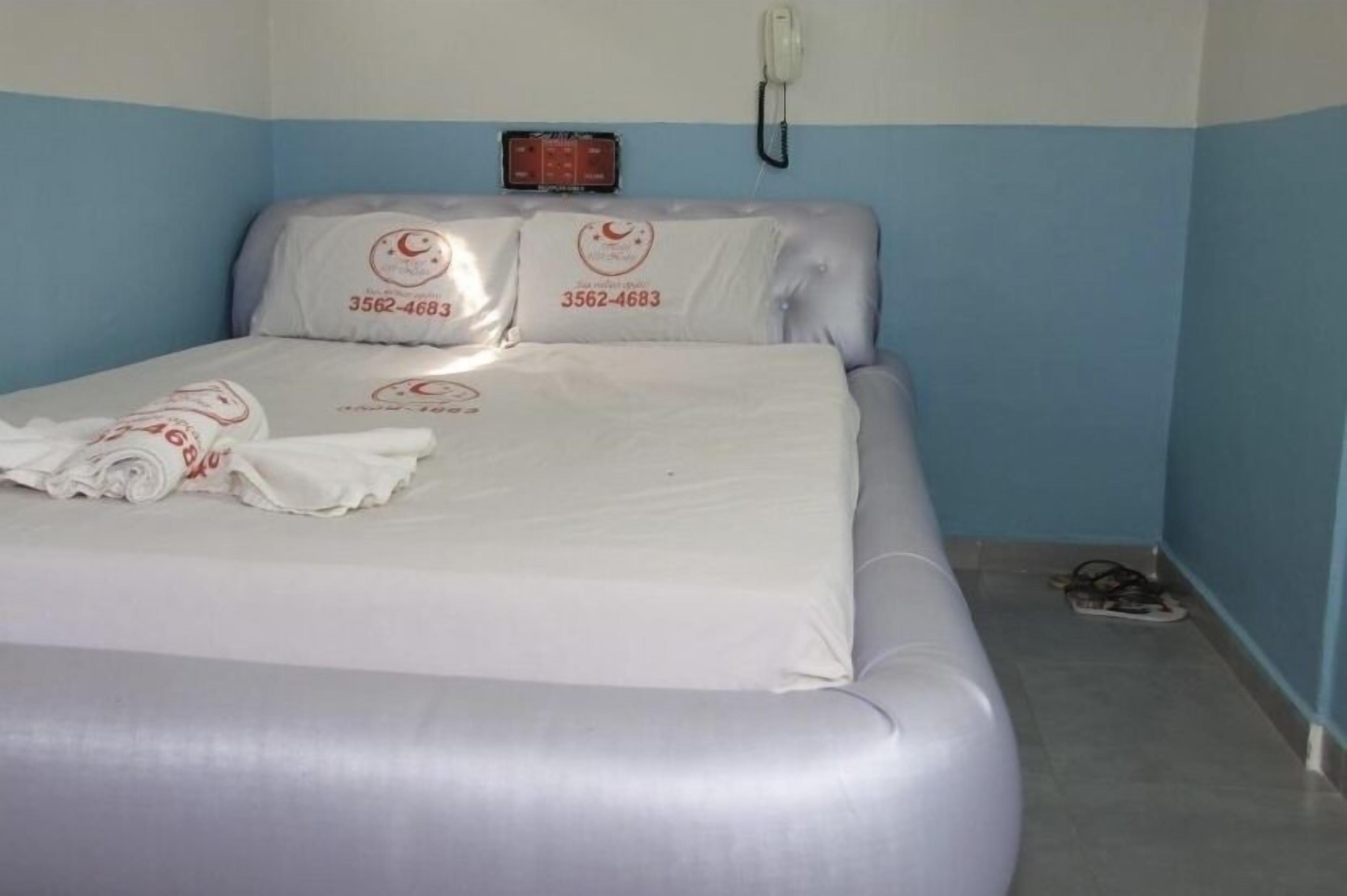 A neatly made bed with white linens and pillows, a bedside phone, and a wall-mounted control panel.