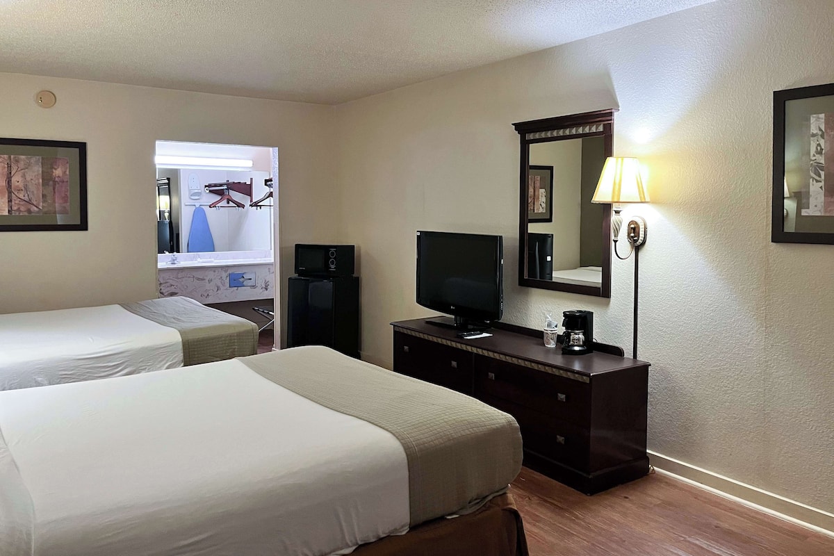 Une chambre d’hôtel avec deux lits, une télévision, une commode et un miroir.