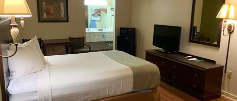 Une chambre d’hôtel avec un lit, un bureau, une télévision et un miroir.