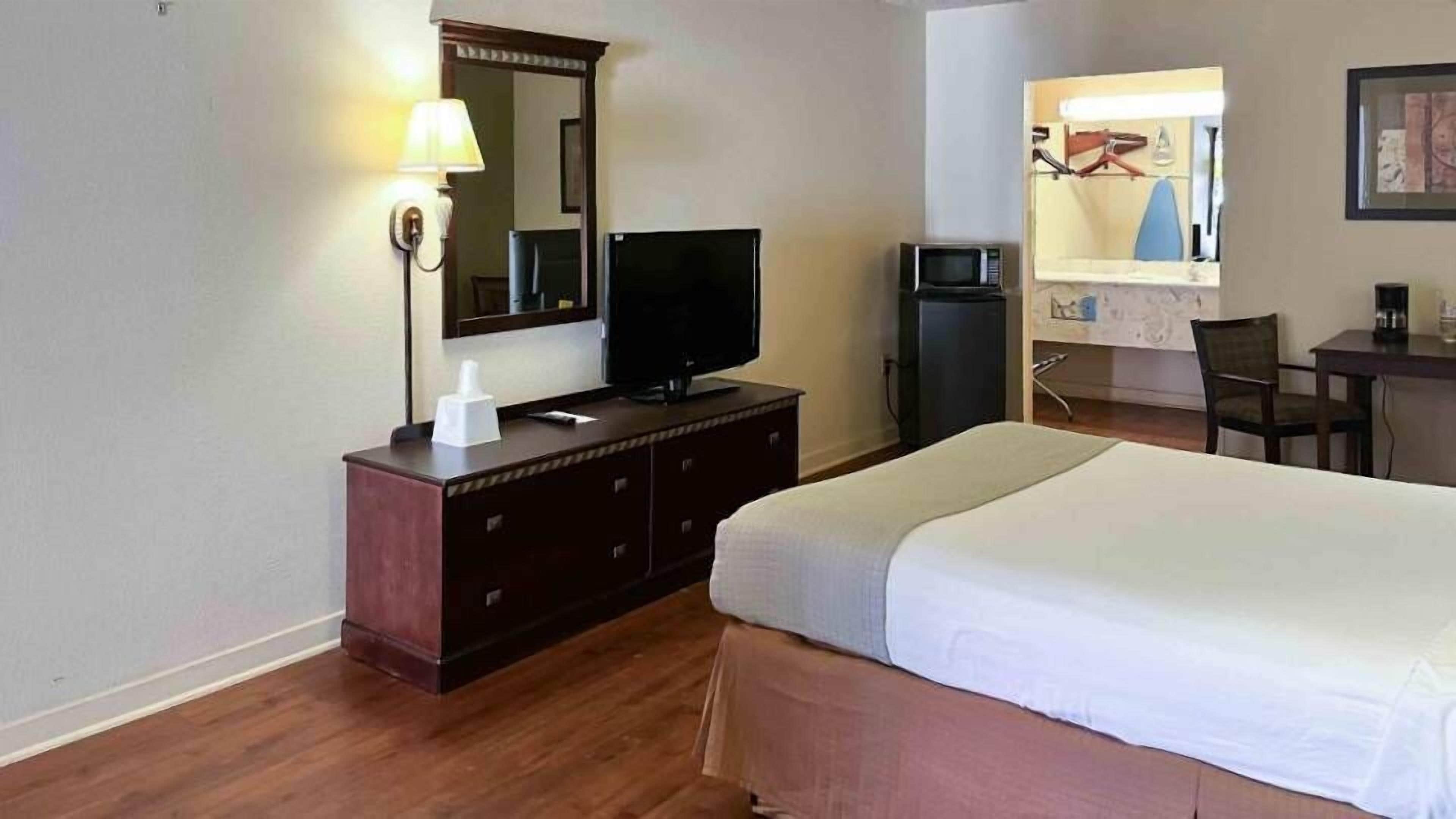 A hotel room with a bed, a TV on a wooden dresser, a microwave, and a desk with a chair.