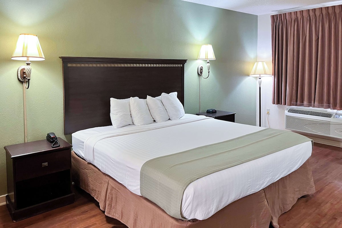 Une chambre d’hôtel avec un grand lit, deux tables de chevet, une petite table d’appoint, un téléphone fixé au mur et un appareil de climatisation.