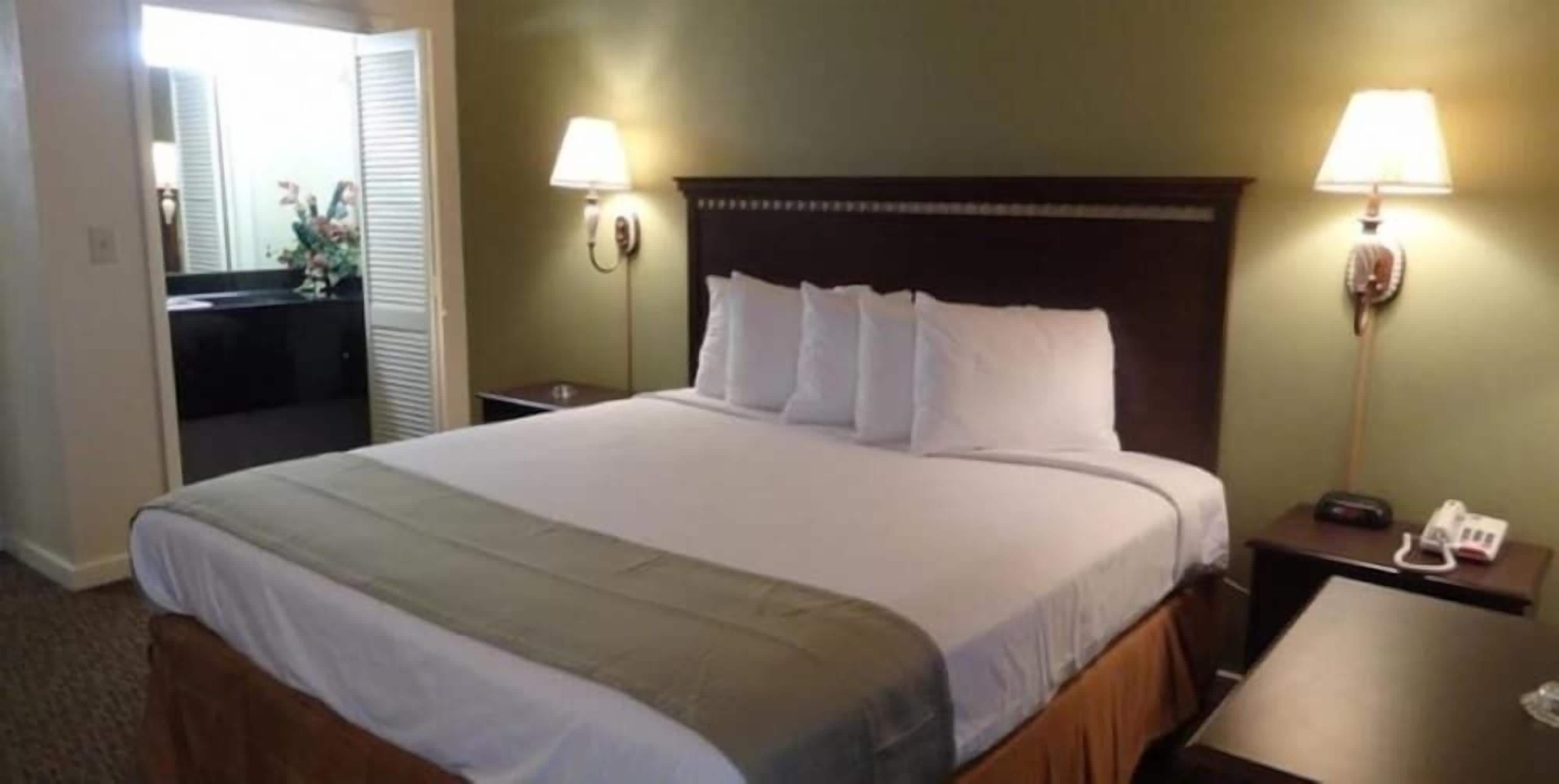 Habitación de hotel con una cama grande, dos lámparas de noche, una mesita de noche con teléfono y un espejo.