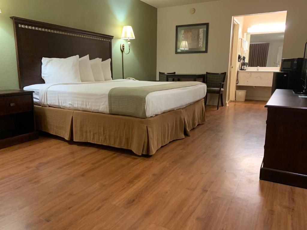 Une chambre d’hôtel avec un grand lit, une table de chevet, une lampe, un bureau, une chaise et un petit coin cuisine.