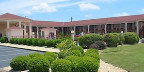 A multi-story building with a red roof, a parking lot, and well-maintained green lawns. - Motel 6 Abbeville, AL (Abbeville)