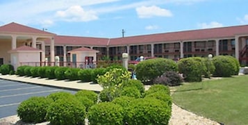 A multi-story building with a red roof, a parking lot, and well-maintained green lawns.