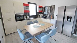 A modern kitchen with a dining area, featuring a wooden table, blue chairs, and a refrigerator. - Attractive holiday house near the sea! (Vinjerac)