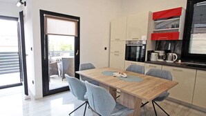 A modern kitchen with a wooden table, grey chairs, and a sliding glass door leading to an outdoor seating area. - Attractive holiday house near the sea! (Vinjerac)