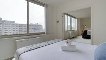 A hotel room with a large window, a bed with a white duvet, and a radiator.