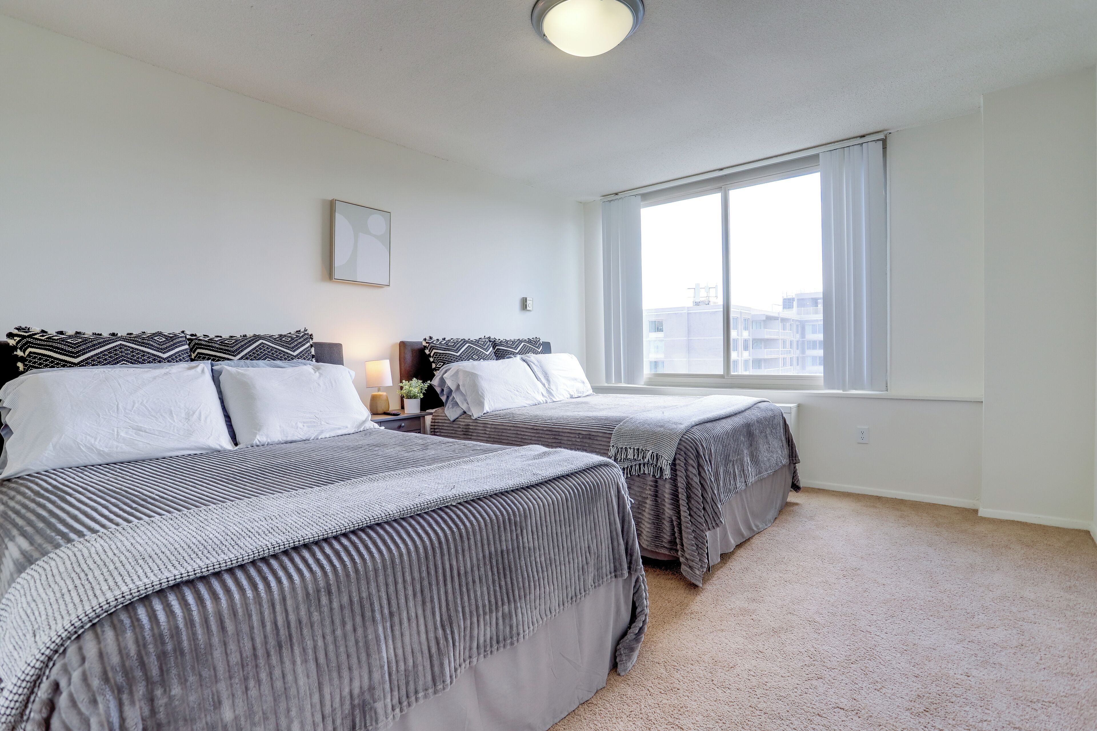 A bedroom with two beds, a large window, and a ceiling light.