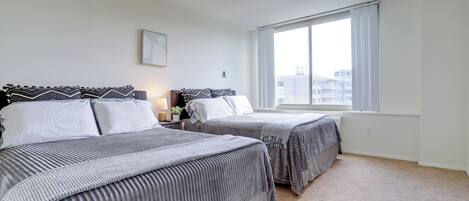 A bedroom with two beds, a large window, and a ceiling light.