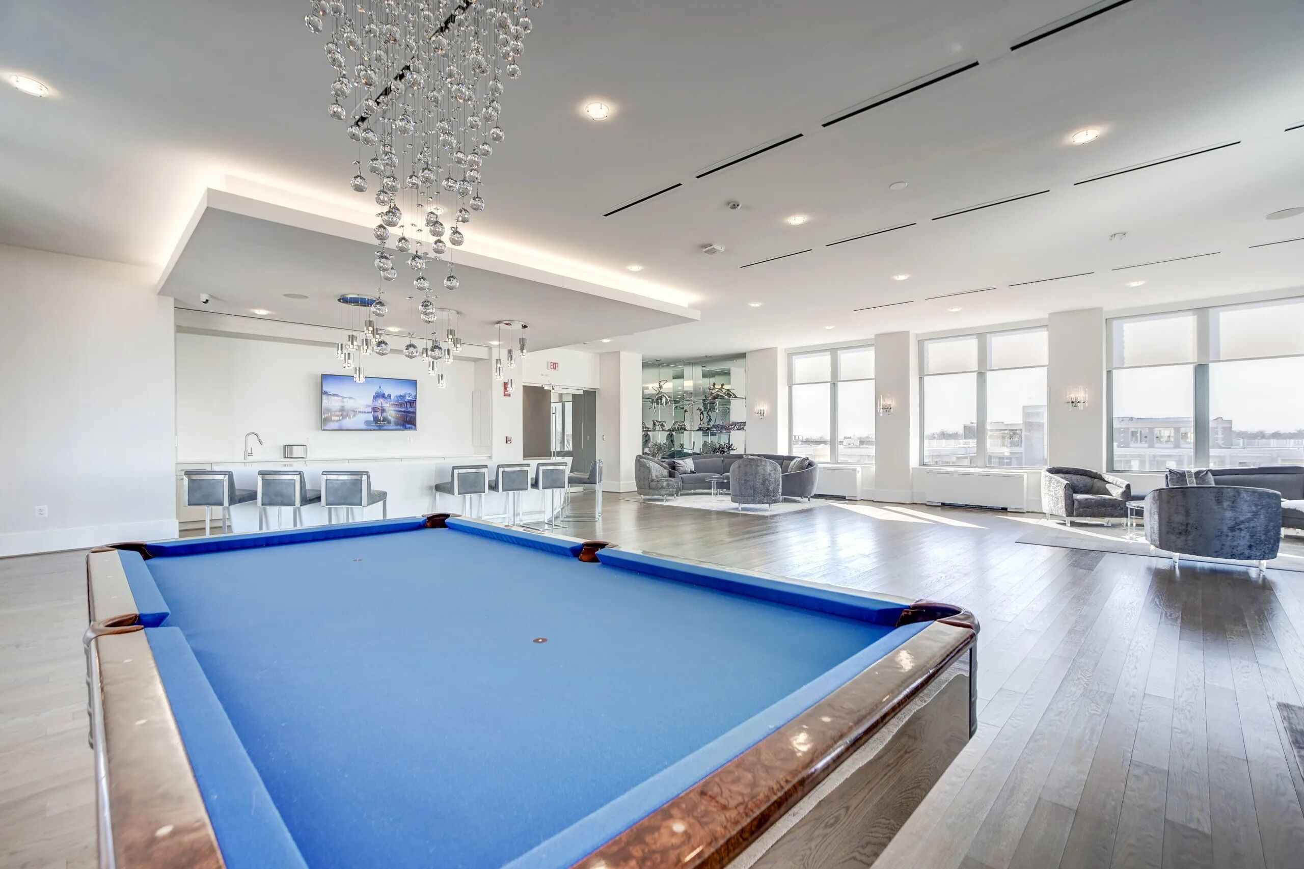 Een modern binnenzwembad met een blauwe pooltafel, comfortabele zitplaatsen en grote ramen met uitzicht op de stad.