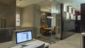 A modern office space with a glass partition, a desktop computer, and a meeting room visible through the partition. - Crystal City Apartments near Crystal Park - We Host (Arlington)