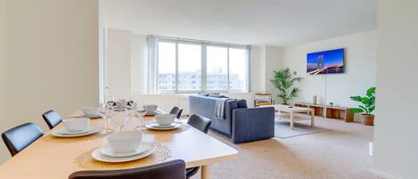 Ein modernes Wohnzimmer mit Essbereich, großen Fenstern und Blick auf die Stadt.