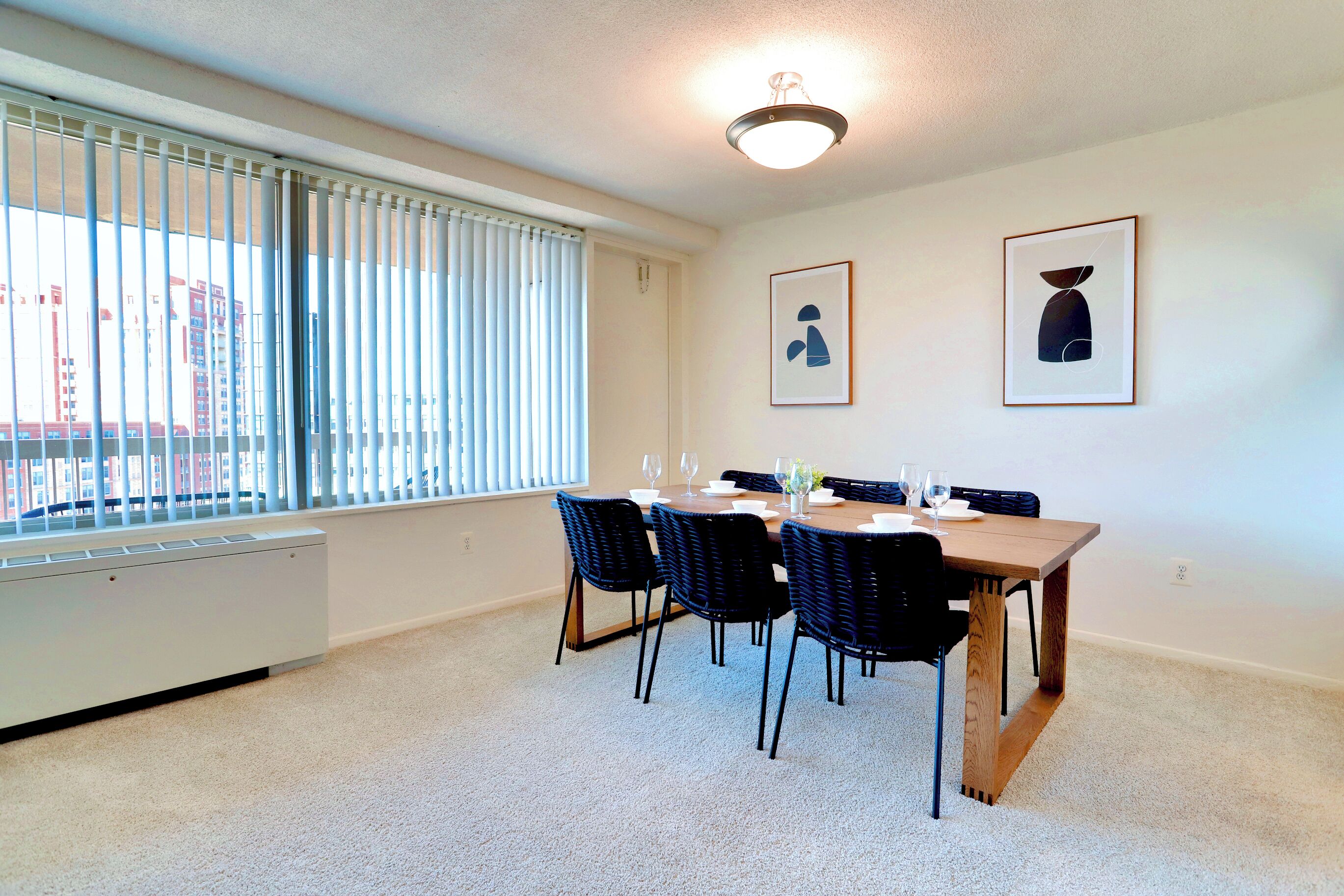 A dining area with a table set for four, black chairs, and a radiator under a window with blinds.
