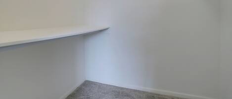 A corner of a room with a white wall, a grey carpet, and a white shelf unit with black brackets.